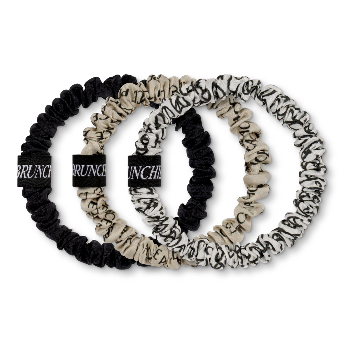 Ein Set aus drei Brunchies aus reiner Seide mit Peace-Prints in beige, weiß und schwarz.